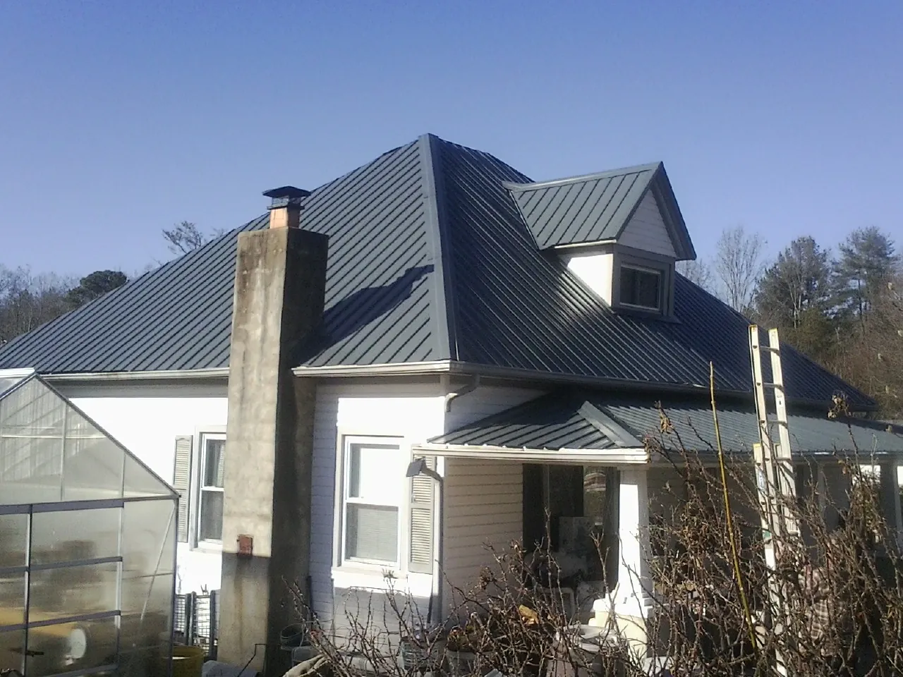 Dark blue standing seam metal roof on a white farmhouse with dormer — Slate & Tile Roof Repair by Roofing Brothers in Mc Grann