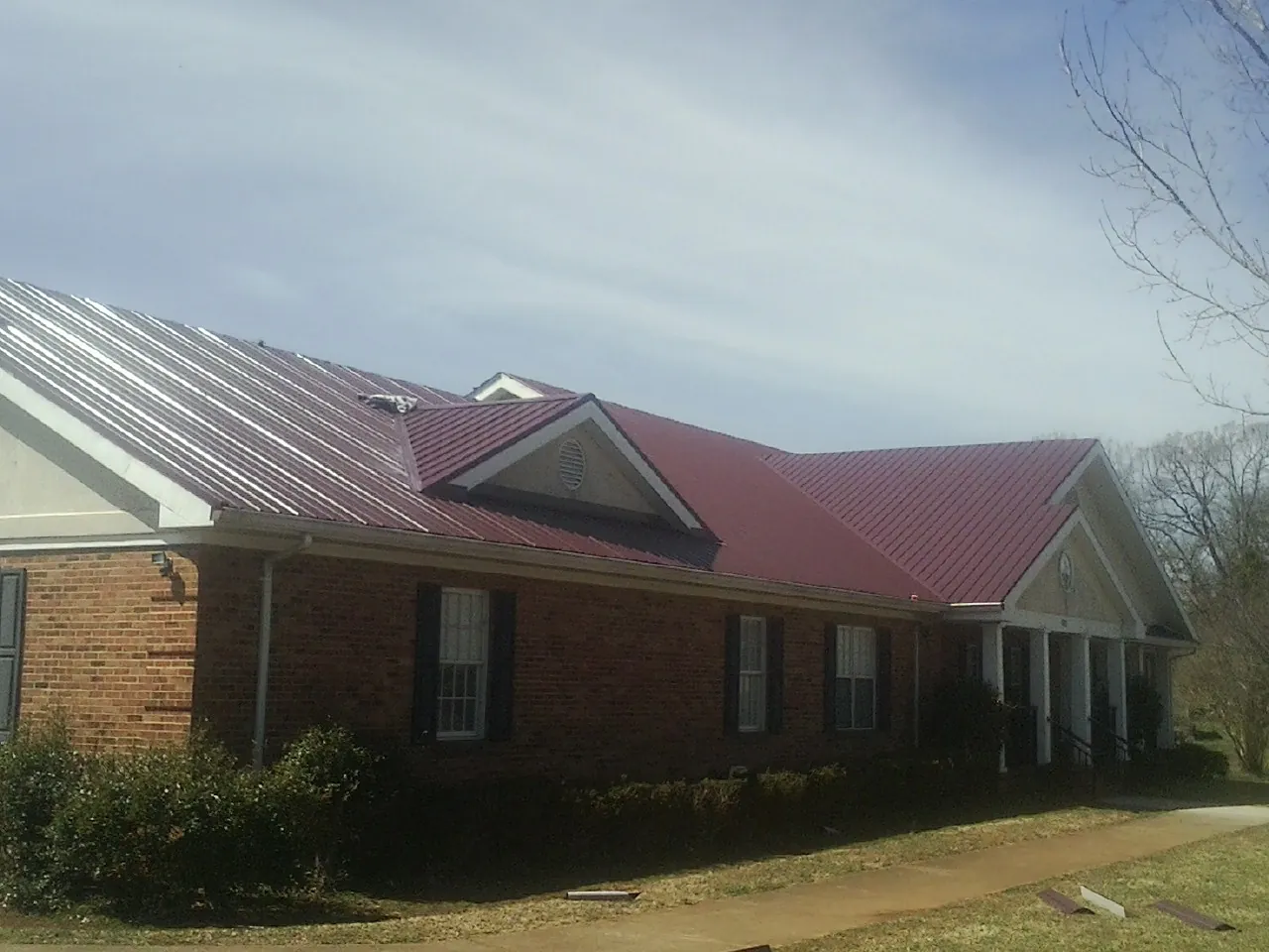 Red metal roof with gabled entries on a long brick building, from a Hail Damage Roof Repair job in Mc Grann