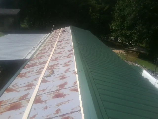 Old rusted panels beside newly installed green metal roofing — Wind Damage Roof Repair by Roofing Brothers in Mc Grann