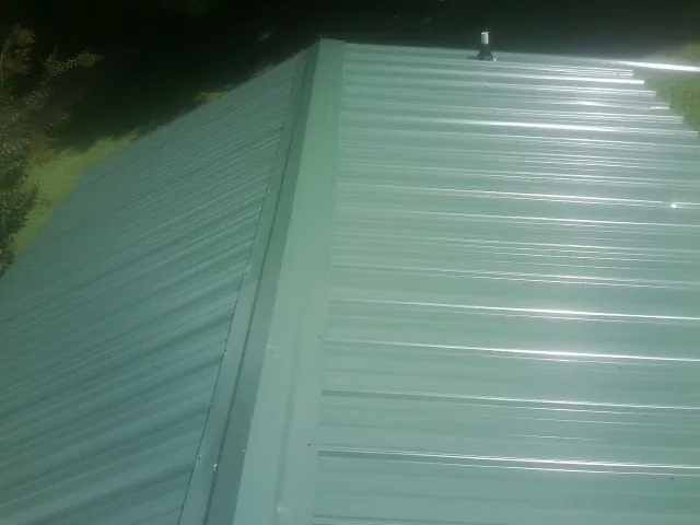 New green metal panels meeting at the ridge of a roof — Flat Roof Repair work by our crew in Mc Grann