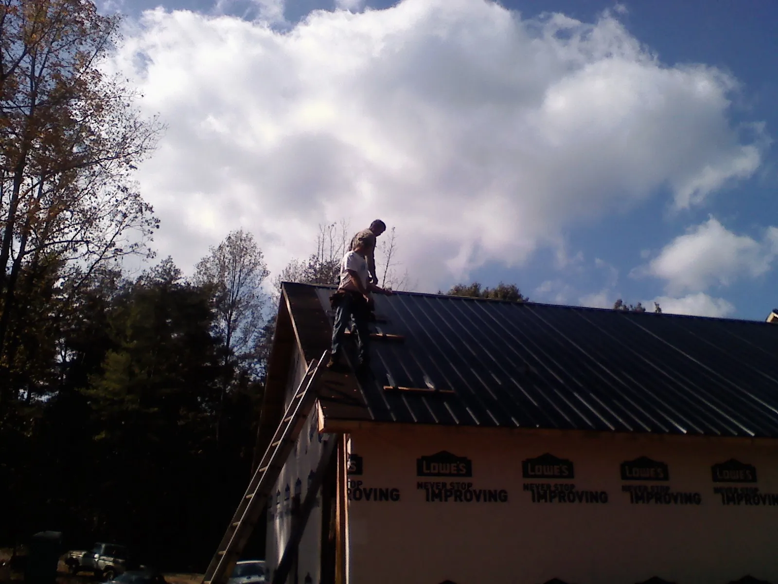 Roofer fastening dark metal panels high against a cloudy sky, from a Roof Inspection job in Mc Grann