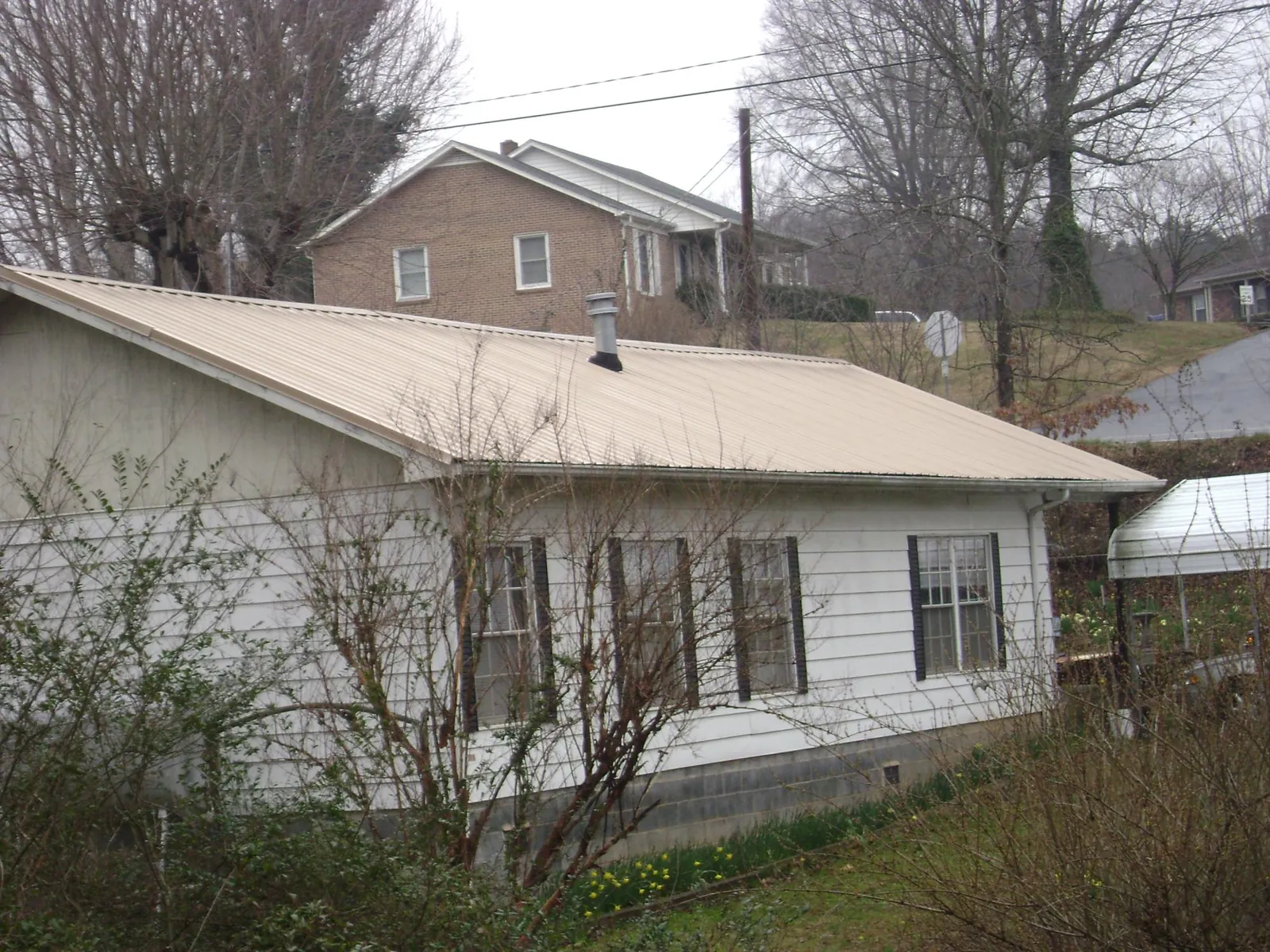 Tan metal roof on a white sided house set into a hillside — Commercial Roofing by Roofing Brothers in Mc Grann