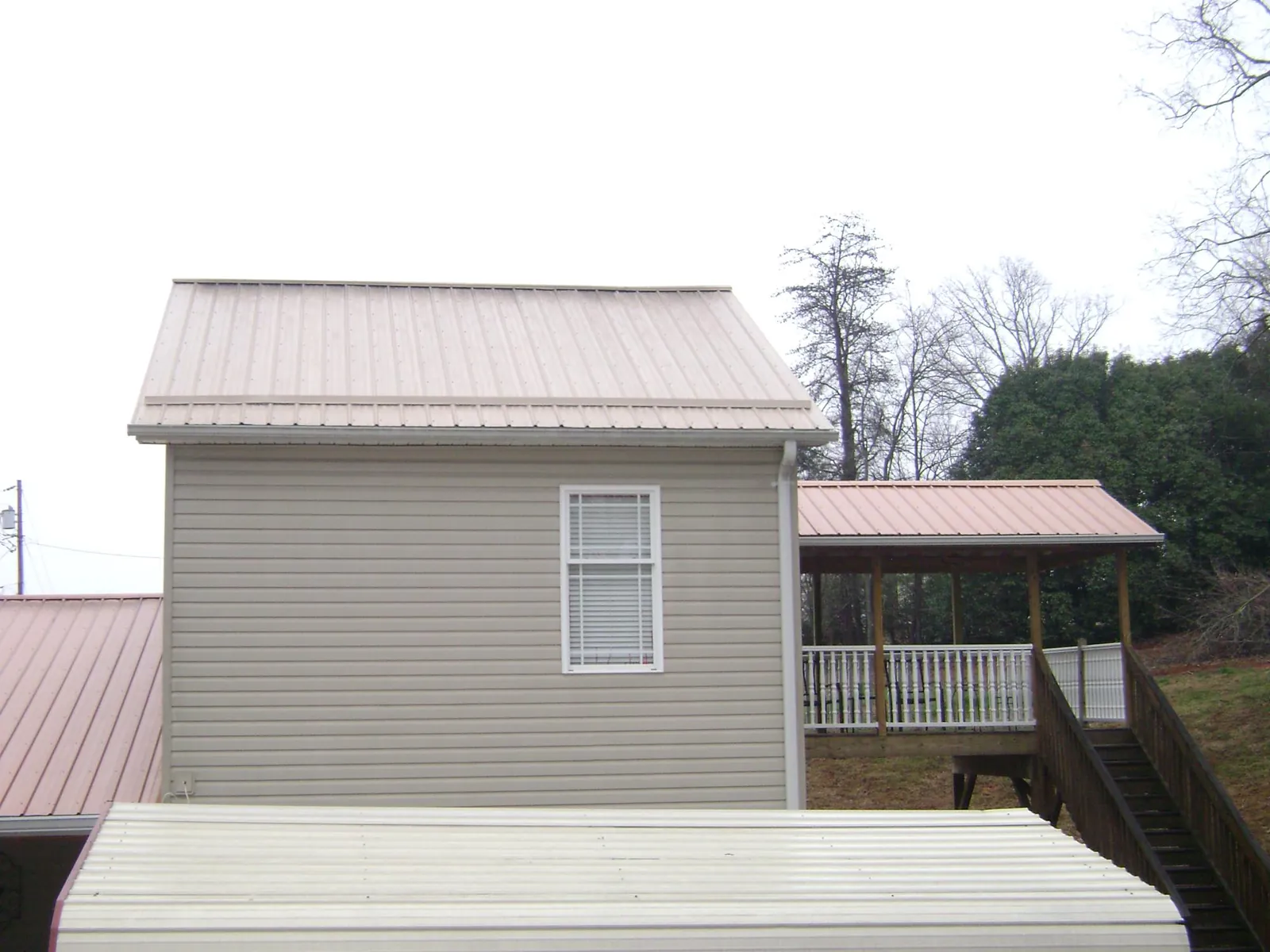 Tan metal roofs on a two story addition and attached porch, from a Roof Replacement job in Mc Grann